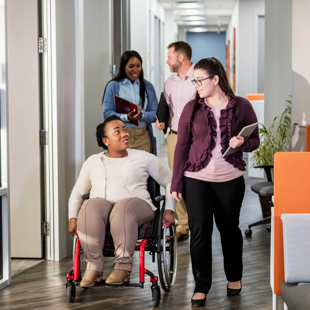 Group of business people talking and walking down an office corridor, one person in a wheelchair